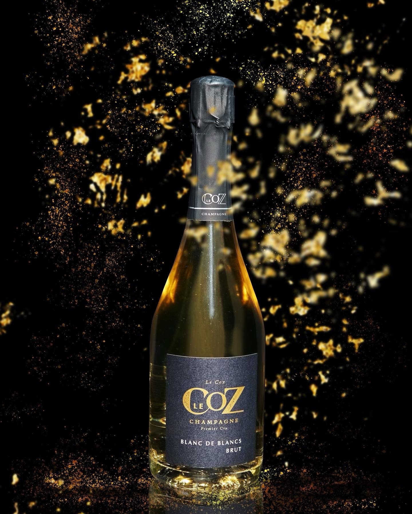 Bouteille de Champagne Le Coz Blanc de Blancs Brut sur fond noir et paillettes dorées